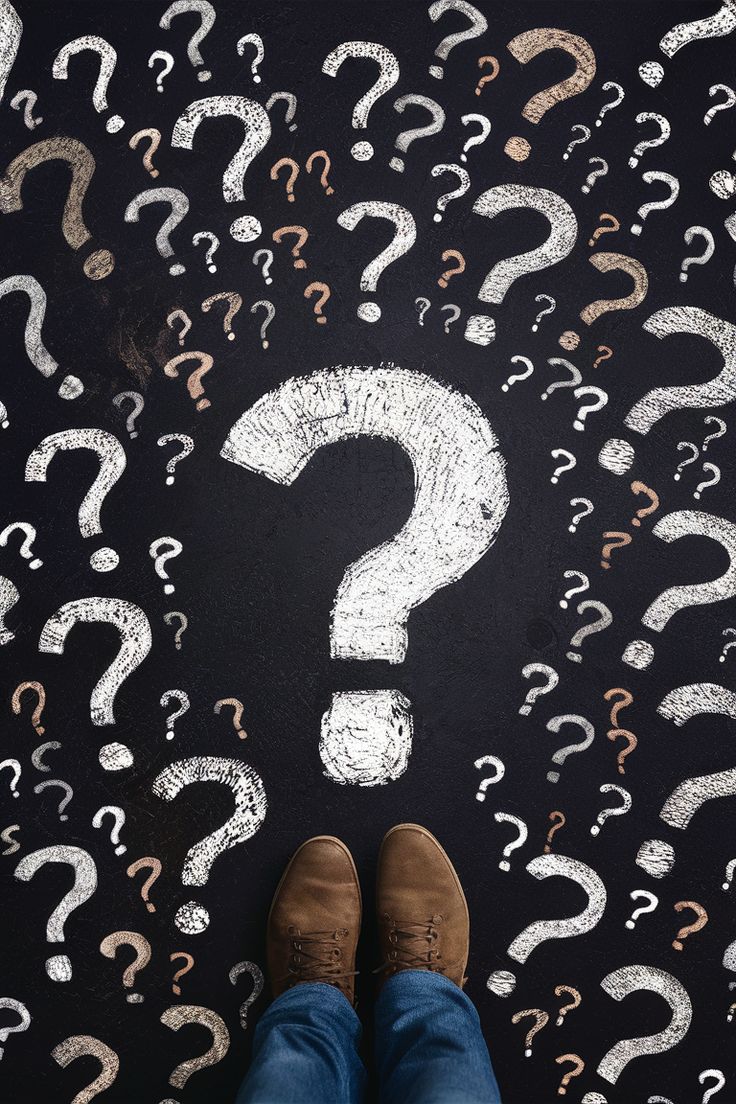 Person standing on a chalkboard-style surface covered in hand-drawn question marks, viewed from above, symbolizing decision-making or uncertainty.