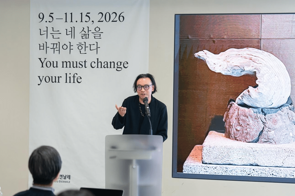 Speaker presenting at an art exhibition in Seoul, standing beside a large artwork with text about changing your life.