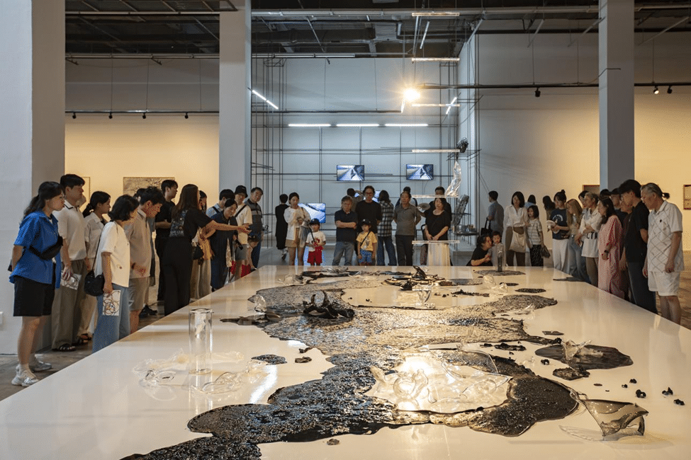 visitors gathered inside a contemporary art gallery around a large installation spread across the exhibition floor.