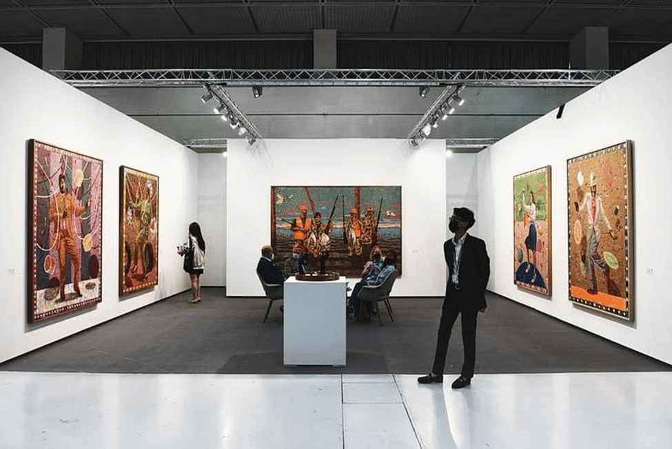 Art gallery booth displaying large contemporary paintings on white walls, with visitors viewing the artworks.