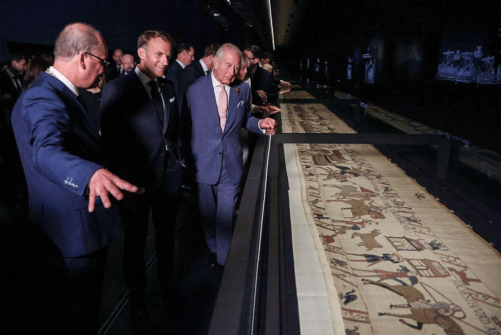 Visitors viewing the Bayeux Tapestry in a museum exhibition, with the historic textile displayed in a long illuminated case.