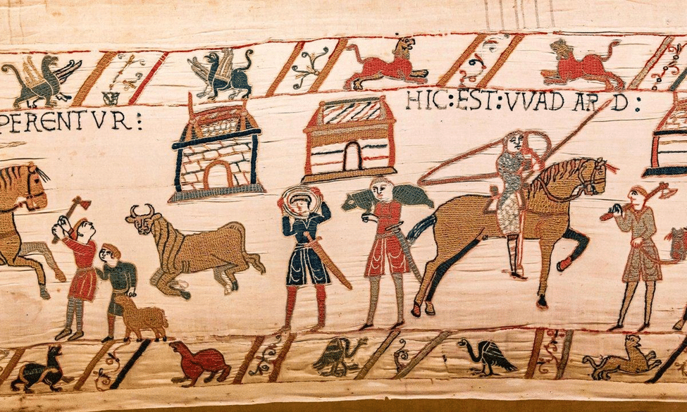 Close-up detail of the Bayeux Tapestry depicting medieval figures, horses, buildings, and Latin inscriptions.