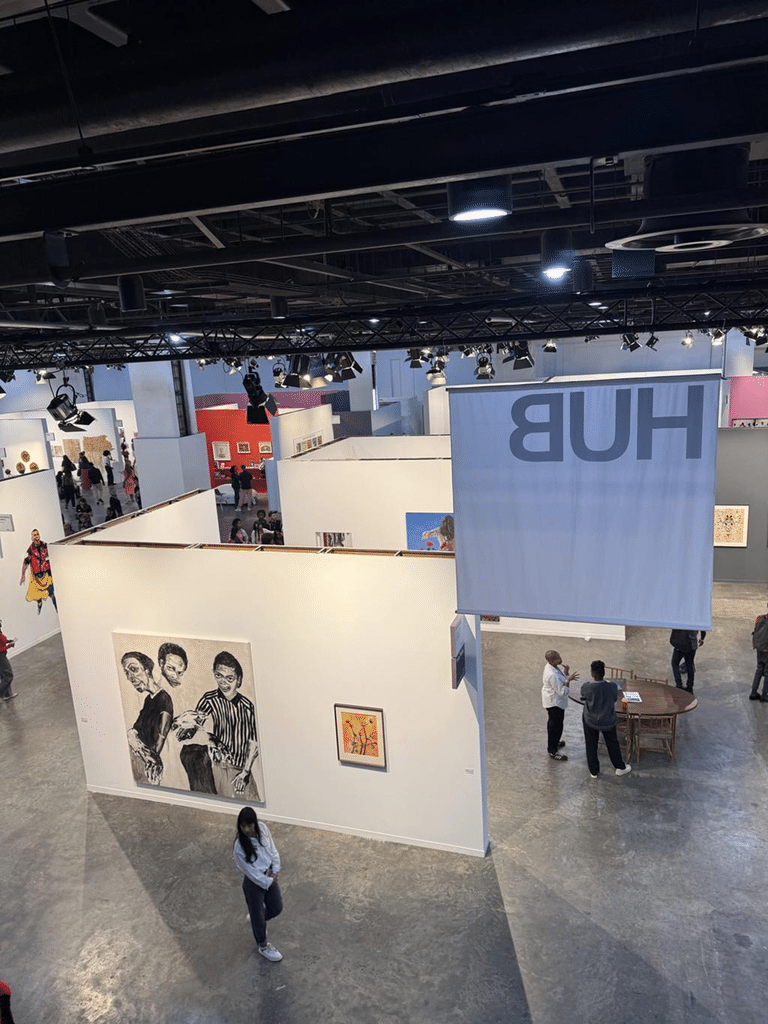 Interior view of an art fair showing multiple gallery booths and visitors viewing artworks.