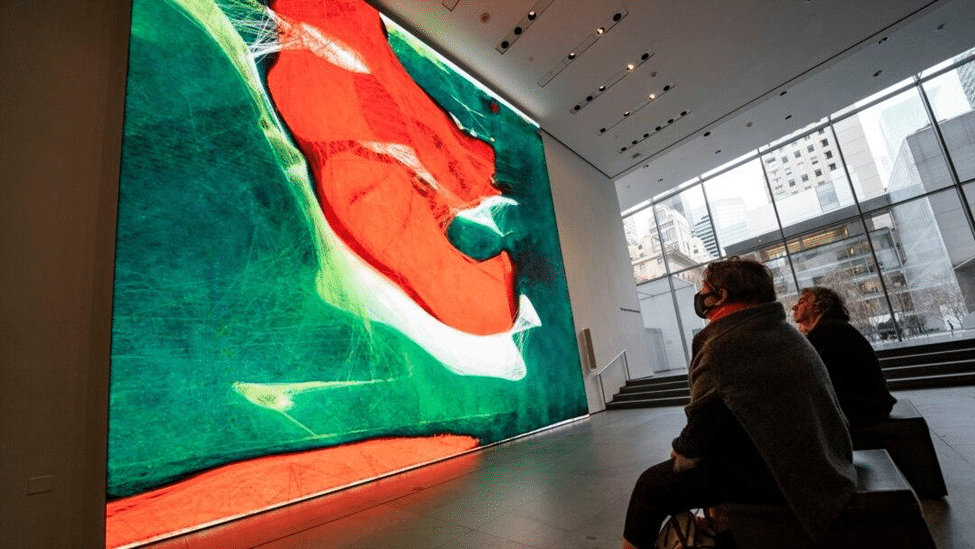 Visitors viewing a large abstract digital artwork in green, red and white displayed on a gallery wall.