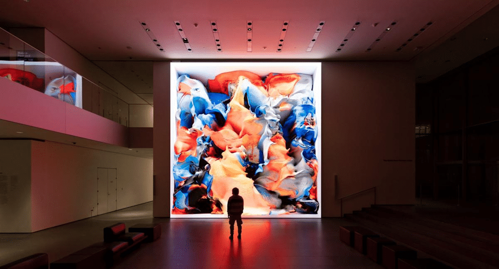 A visitor standing in front of a large colourful abstract digital artwork displayed in a contemporary gallery.