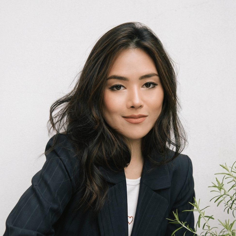 A woman with long dark hair poses for a close-up portrait wearing a dark blazer.
